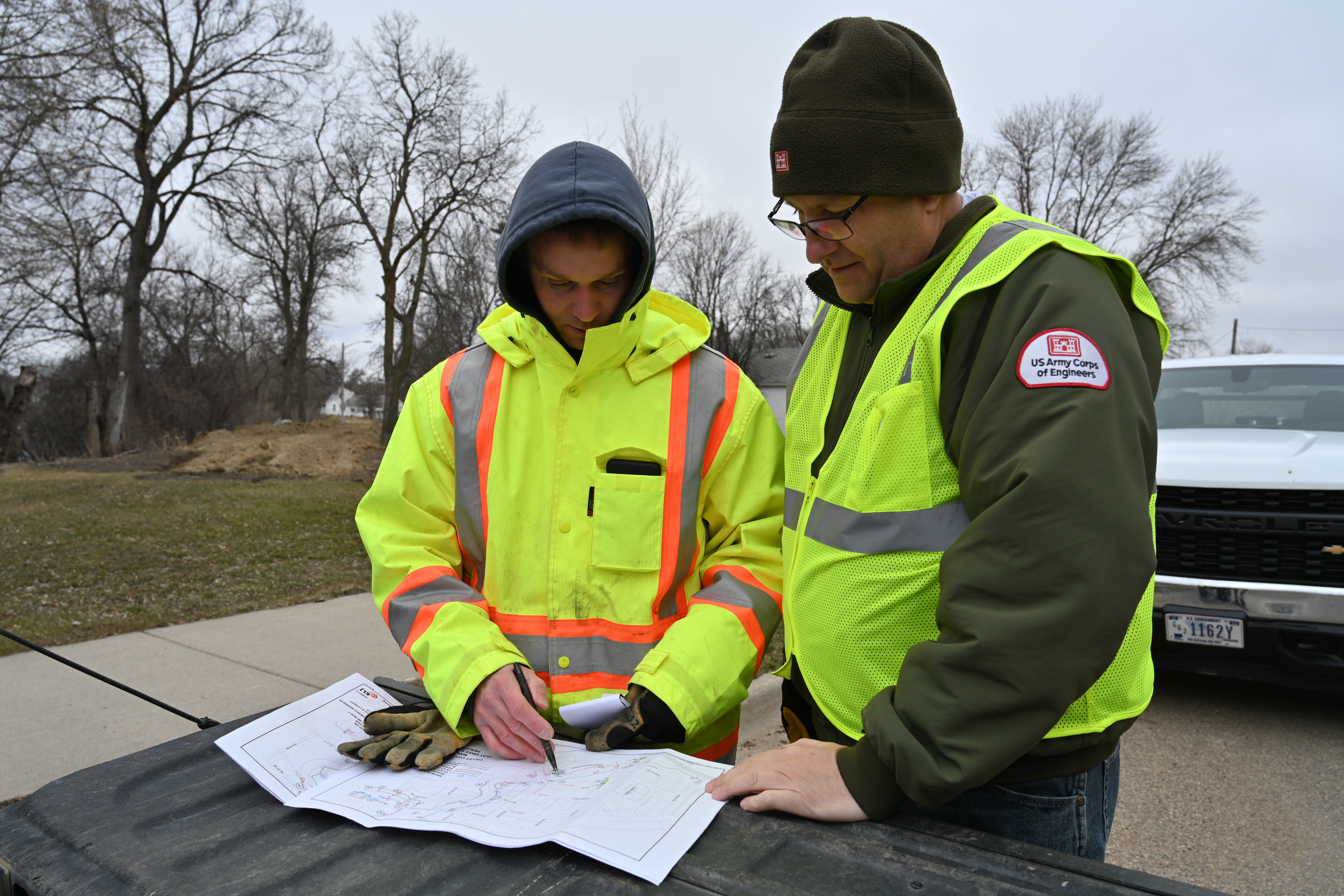 Two men in reflective vests stand outside looking at a large piece of paper