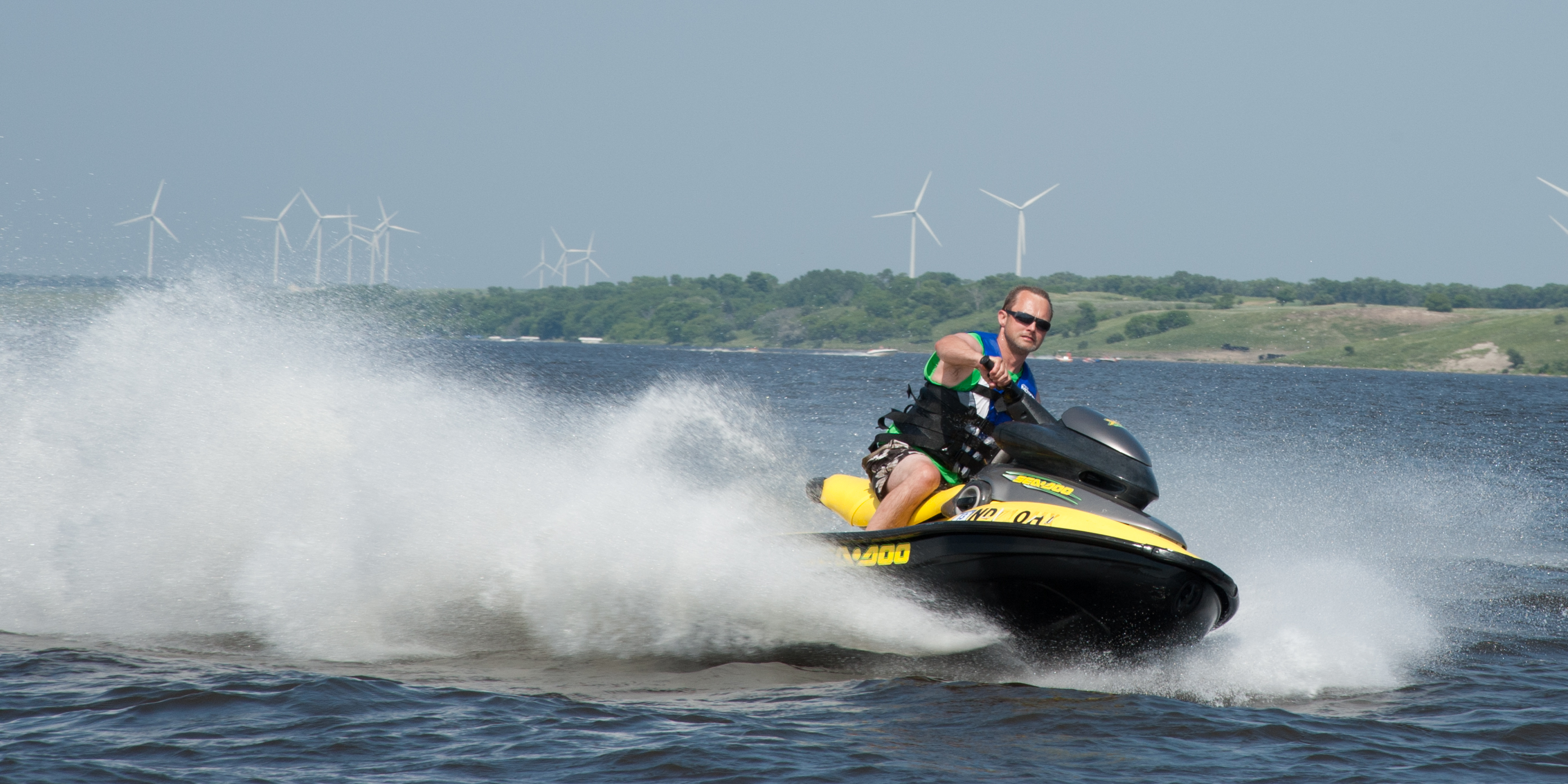 A man on a jetski in the water with wind mills in the background on the land